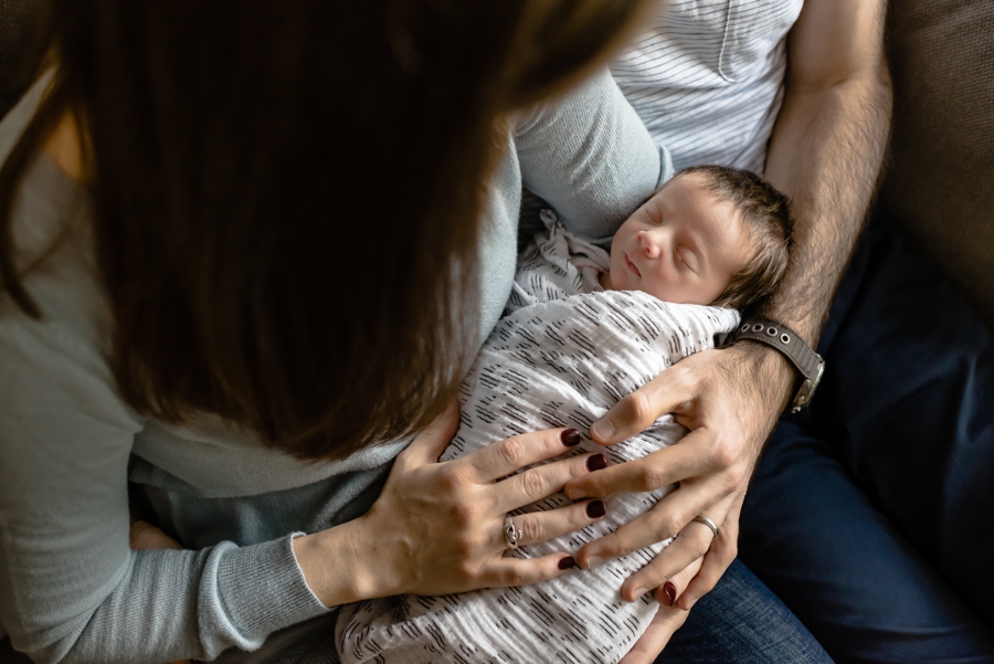 A newborn baby girl sleeps wrapped up in the arms of her mother and father during their newborn family session.